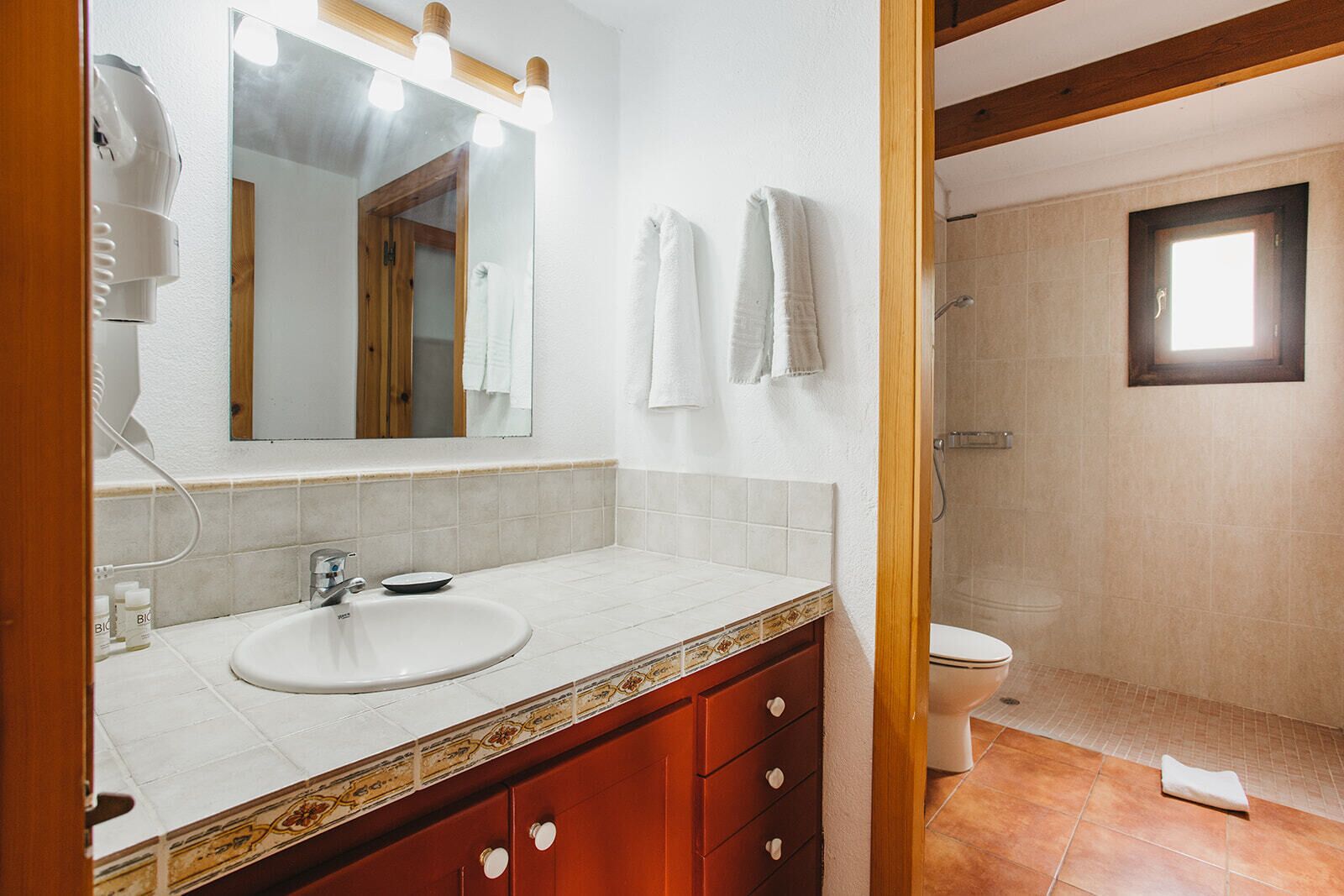 A bathroom with a white sink, wooden vanity, and a shower area.