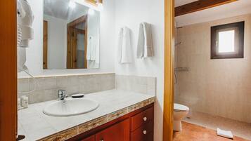 A bathroom with a white sink, wooden vanity, and a shower area.