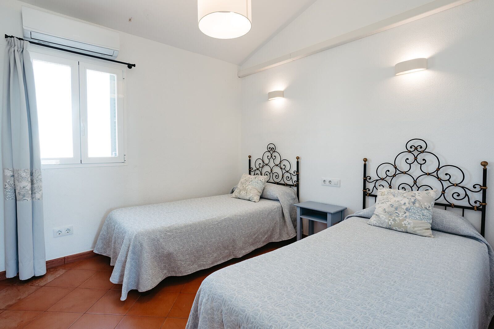 Una habitación con dos camas individuales, una mesita y una ventana con cortinas.