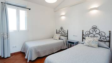 Una habitación con dos camas individuales, una mesita y una ventana con cortinas.