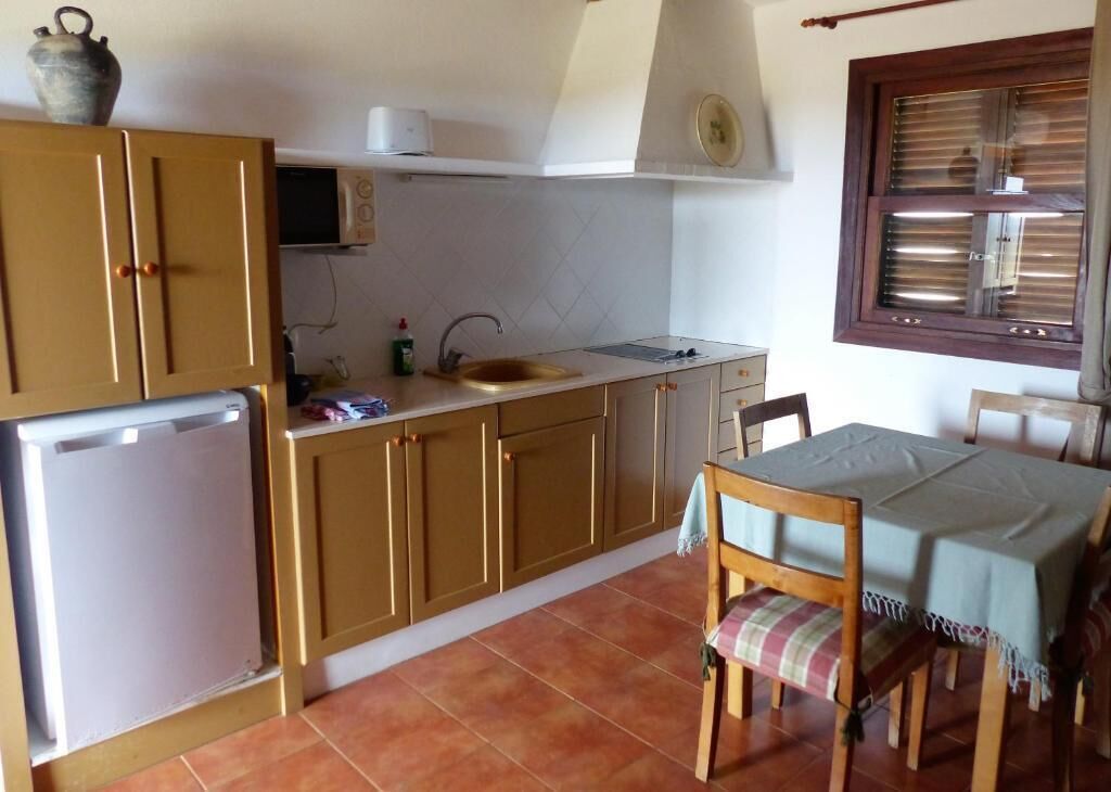 A compact kitchen with wooden cabinets, a sink, a small refrigerator, and a dining area with a table and chairs.