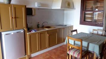 A compact kitchen with wooden cabinets, a sink, a small refrigerator, and a dining area with a table and chairs.