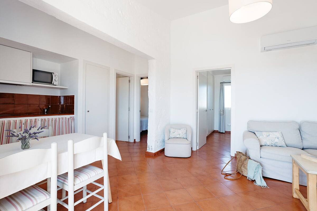 A spacious living area with a white sofa, a dining table with chairs, and a kitchen area with a microwave.