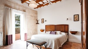Un dormitorio con cabecera de madera, mesita de noche, un banco y vistas al exterior a través de un ventanal.