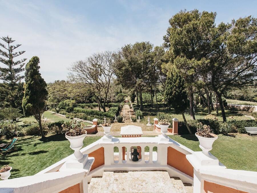 Un vialetto di giardino conduce a una struttura bianca con una fontana, circondata da alberi e piante in vaso.