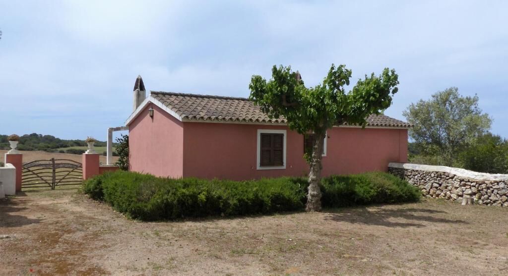 A single-story pink building with a tiled roof, a small window, and a tree in front.