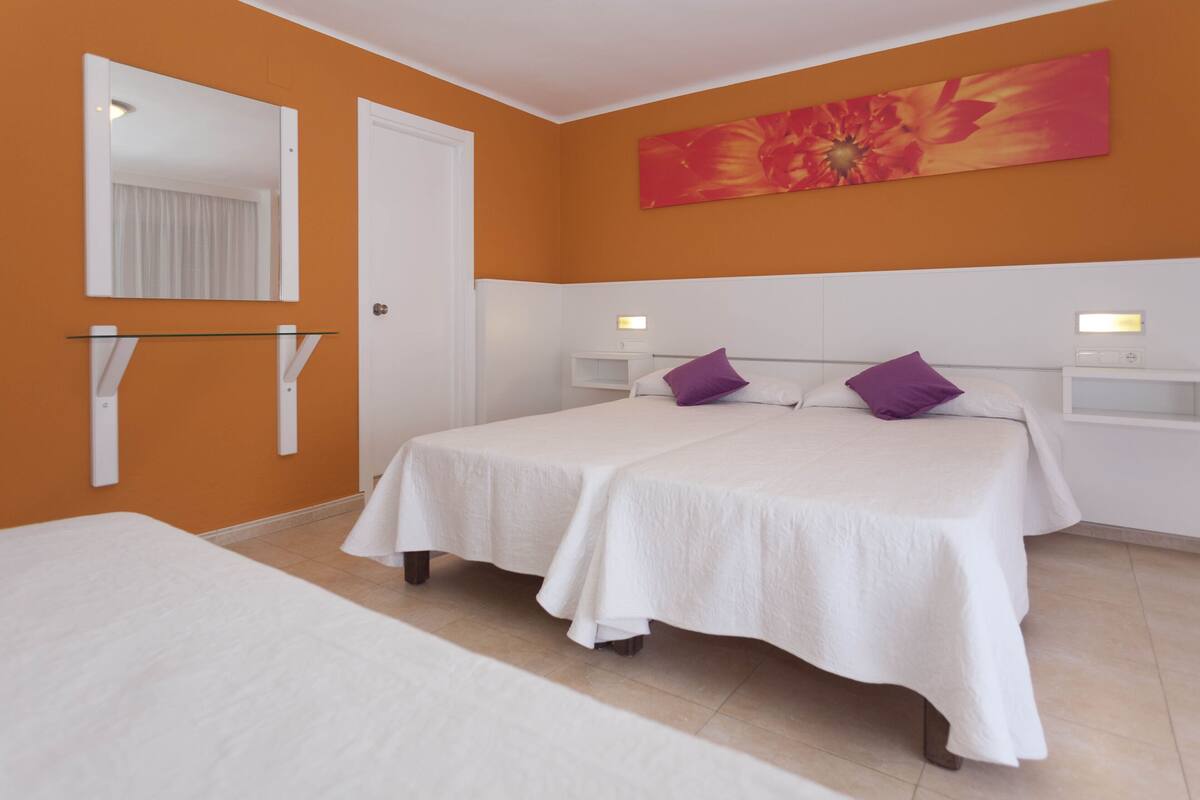 Une chambre avec deux lits, un grand miroir, une œuvre d’art murale et une porte blanche.