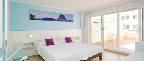 A hotel room with a bed, a glass table, a white desk, a painting of a landscape, and a balcony with chairs.