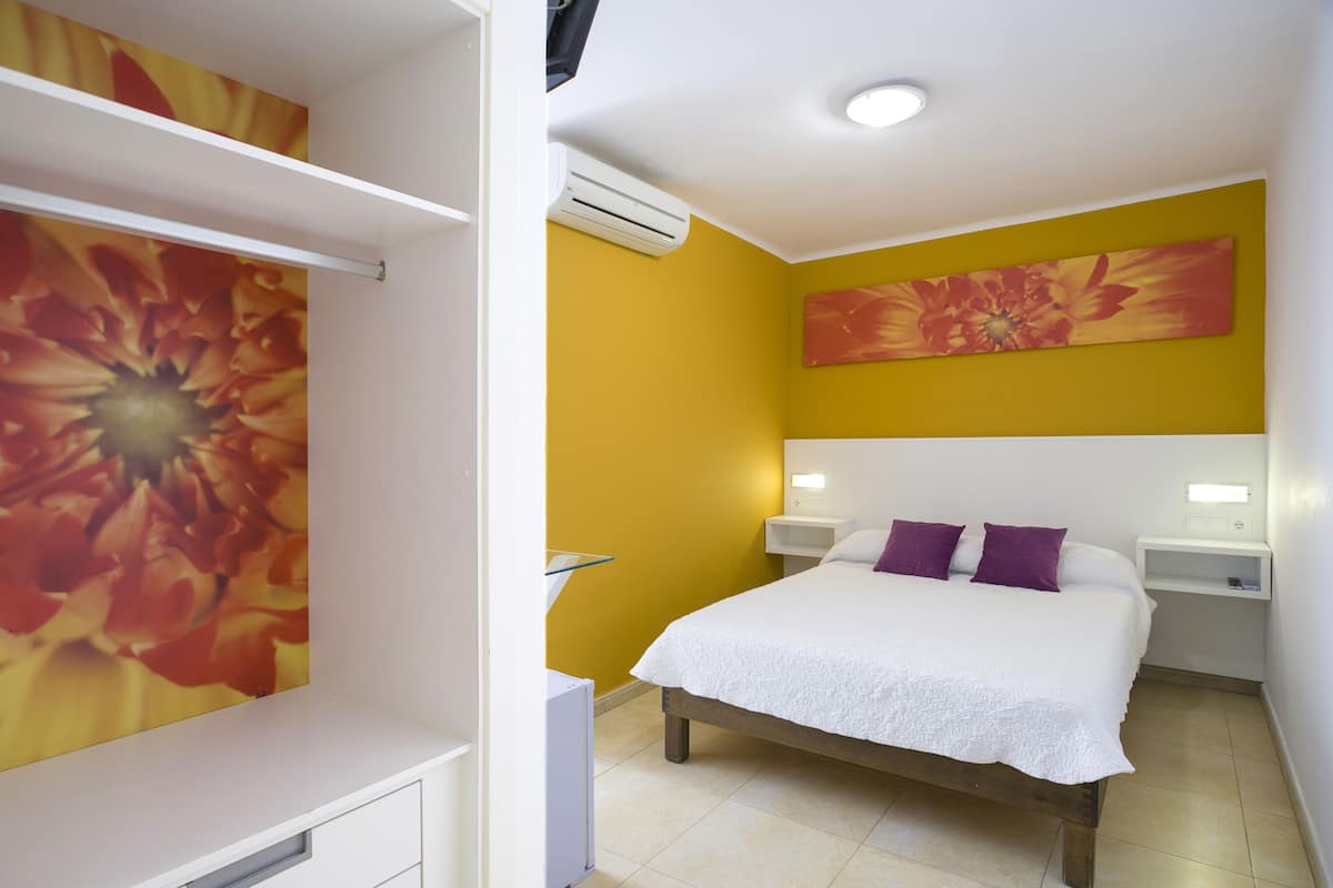 Une chambre à coucher avec un lit, des tables de chevet blanches, une armoire blanche et un mur jaune.
