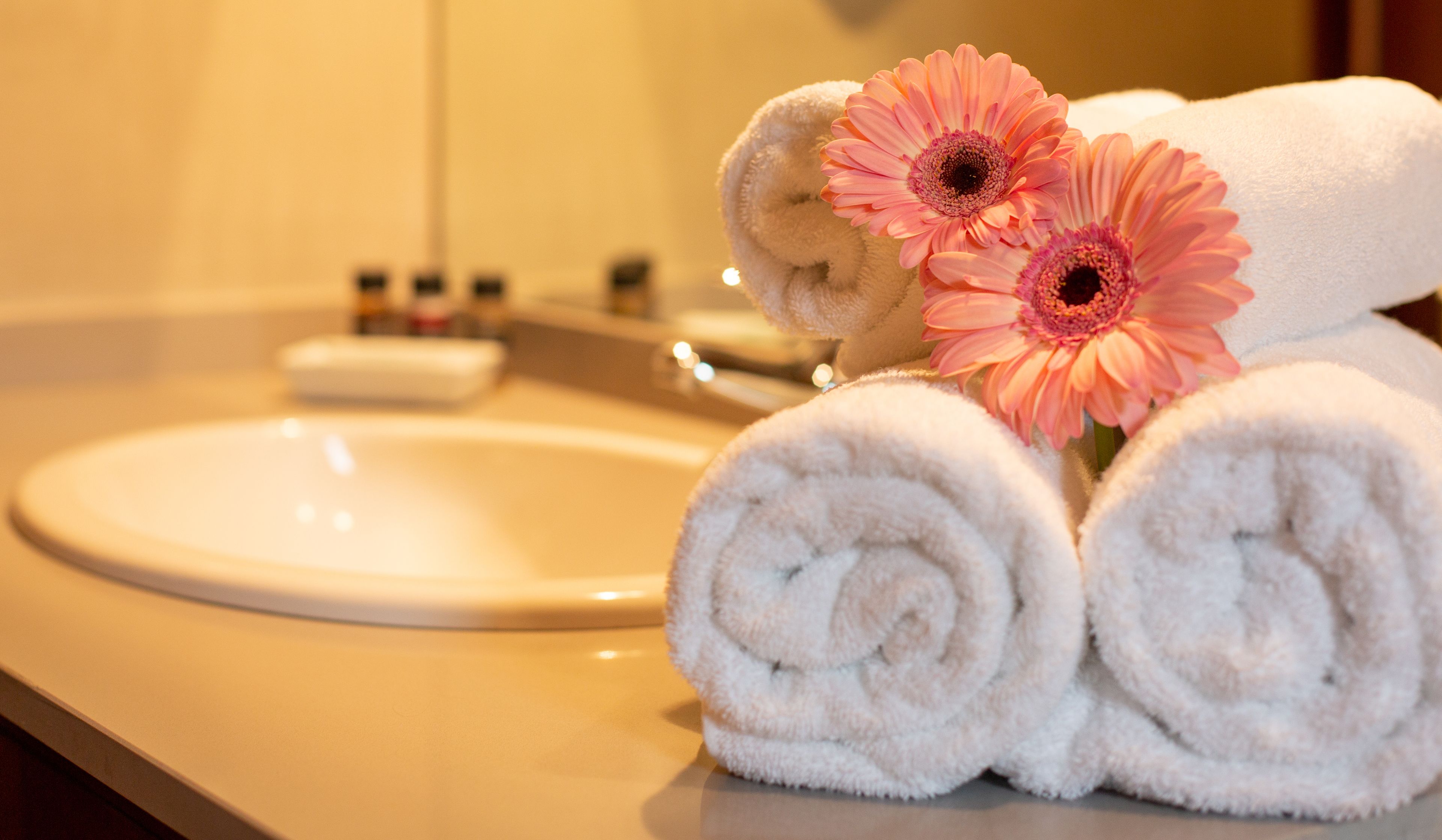 A bathroom with a sink, a mirror, and towels rolled up with pink flowers.