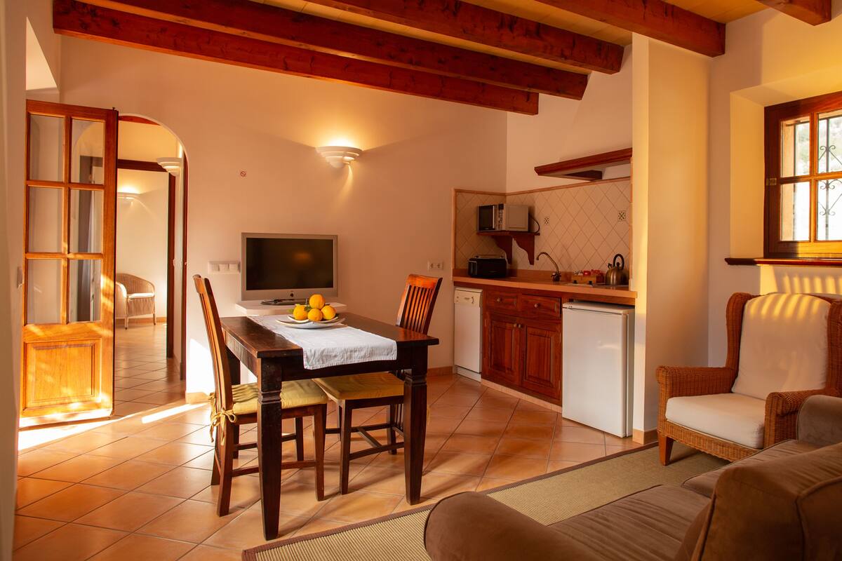 A cozy living room with a sofa, a dining table with chairs, a TV, and a kitchen area with a microwave and kettle.
