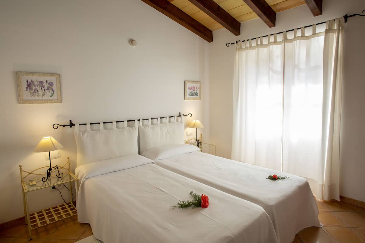 A double bed with white linens, two bedside tables with lamps, and a window with sheer curtains.