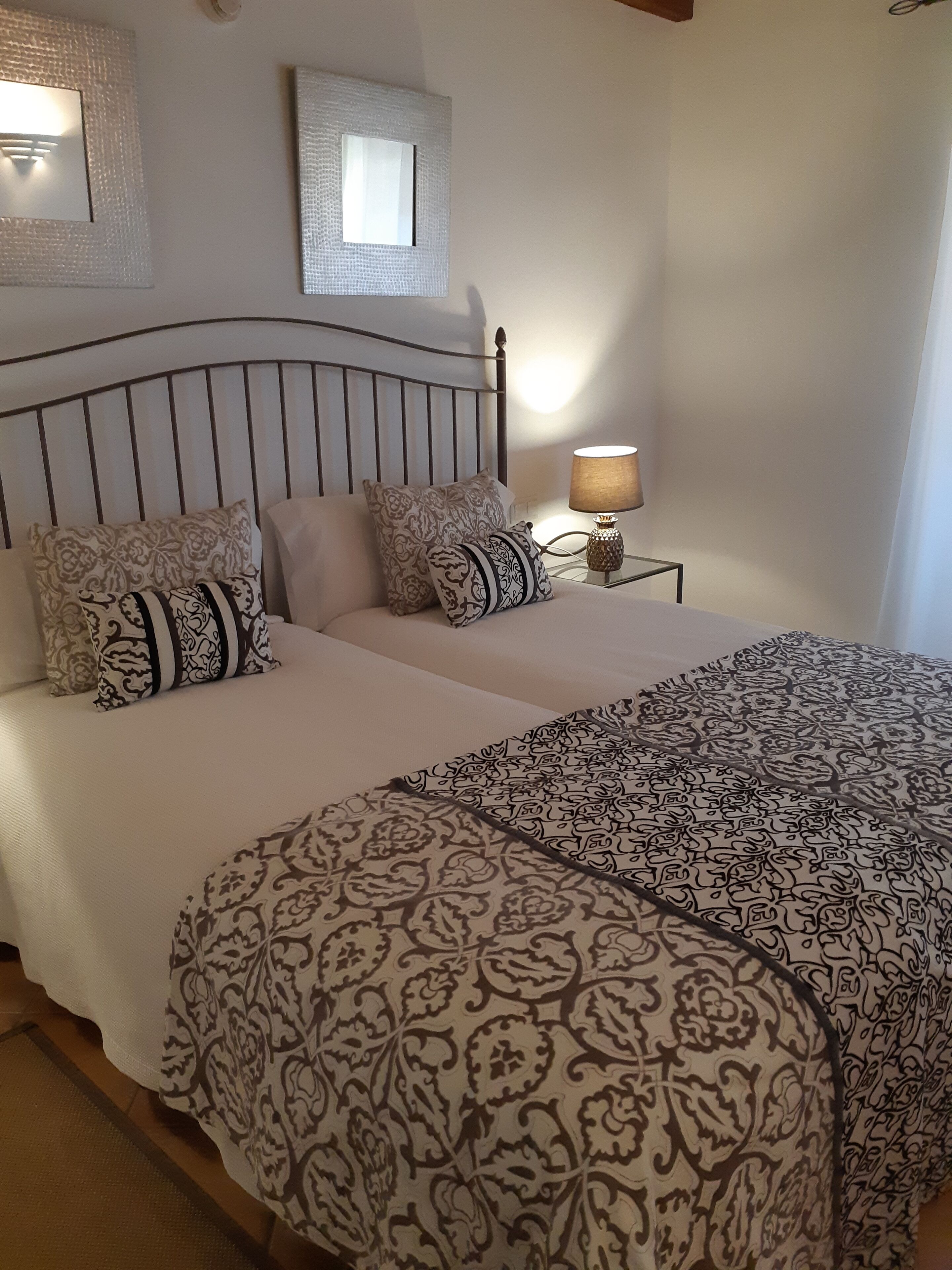 Una cama doble con ropa de cama estampada, una mesita de noche con lámpara y un espejo en la pared.