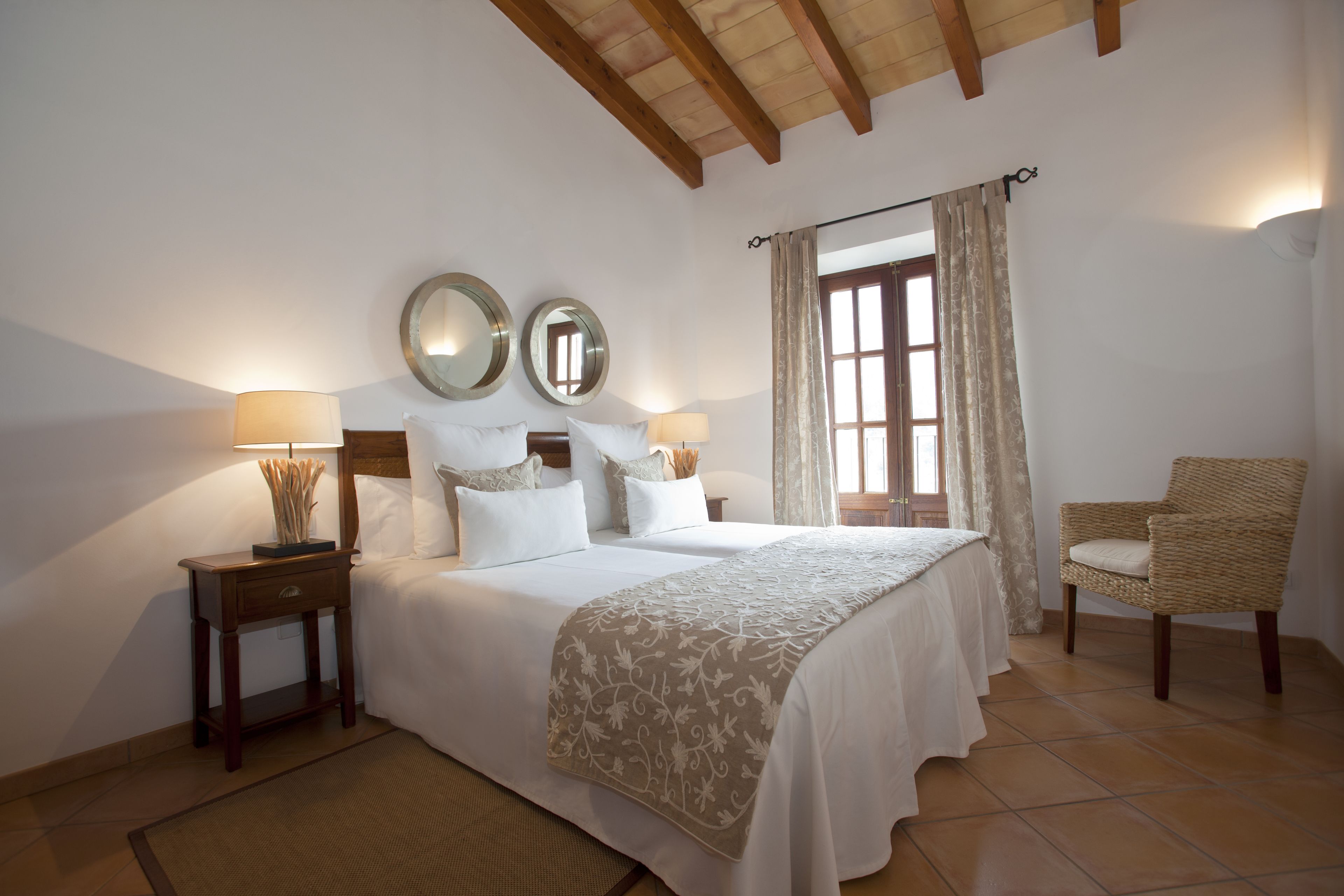 A bedroom with a large bed, two bedside tables, a chair, and a window with curtains.