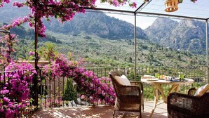 Una terraza con mobiliario de mimbre, una mesa y sillas, con vistas a un paisaje montañoso.