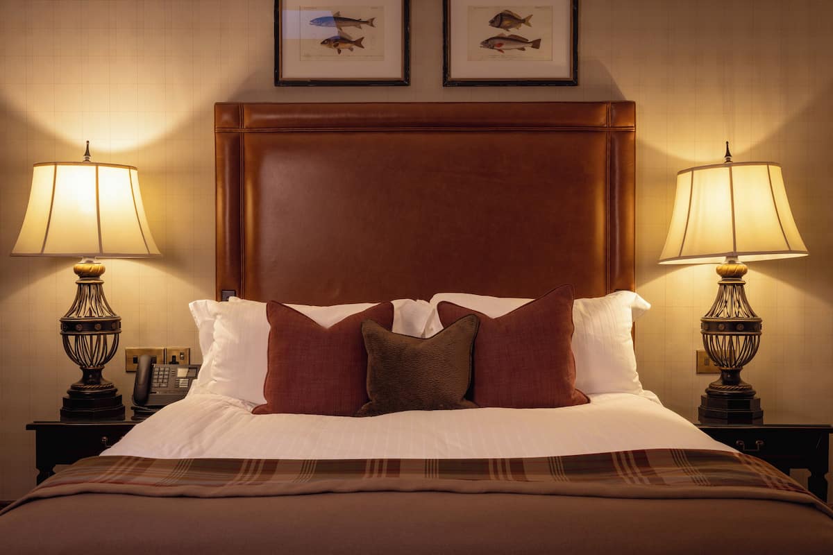 A hotel room with a large bed, two bedside lamps, a telephone, and framed fish illustrations on the wall.