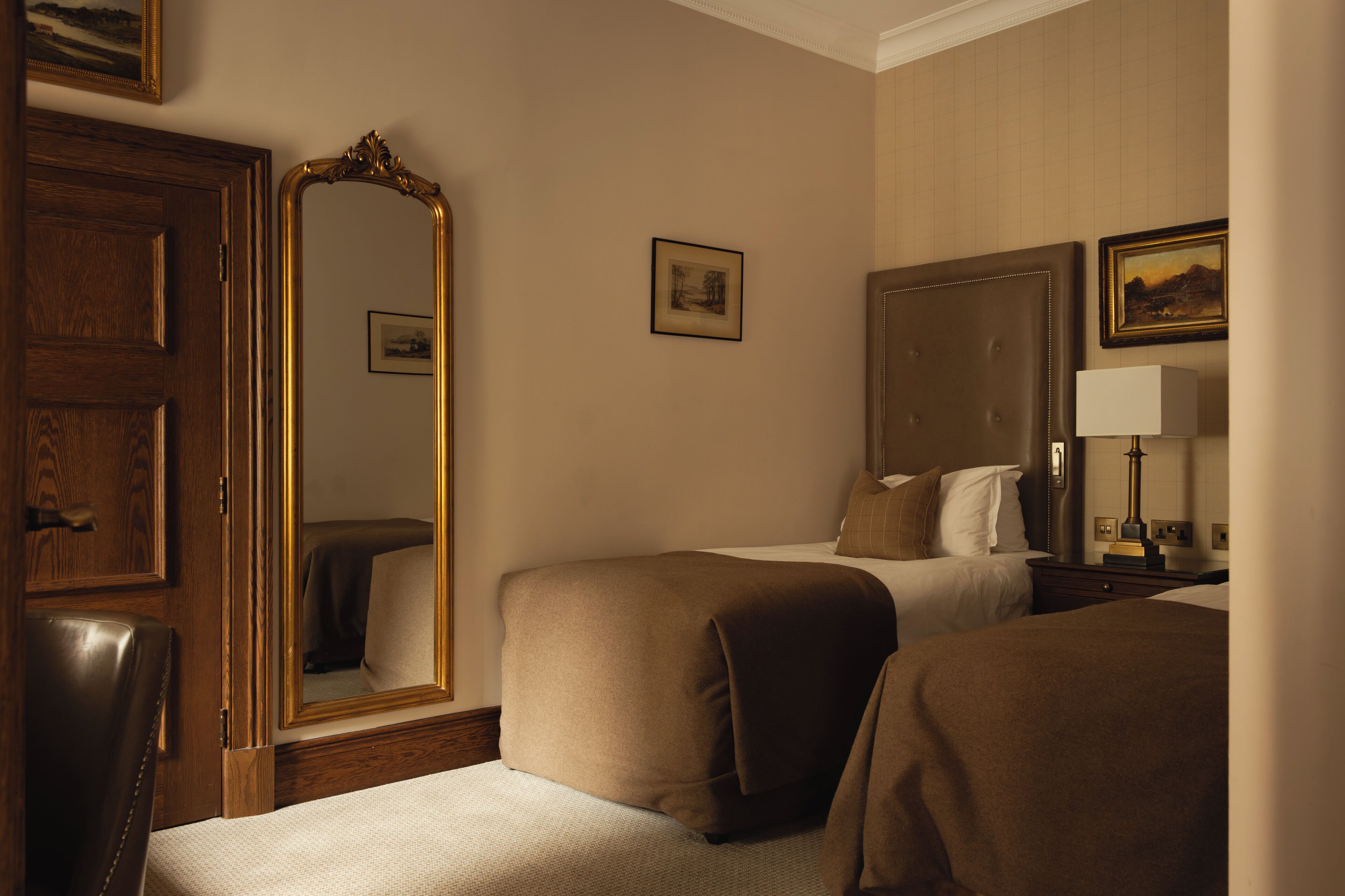 Une chambre d’hôtel avec deux lits, une porte en bois, un grand miroir et une table de chevet avec une lampe.
