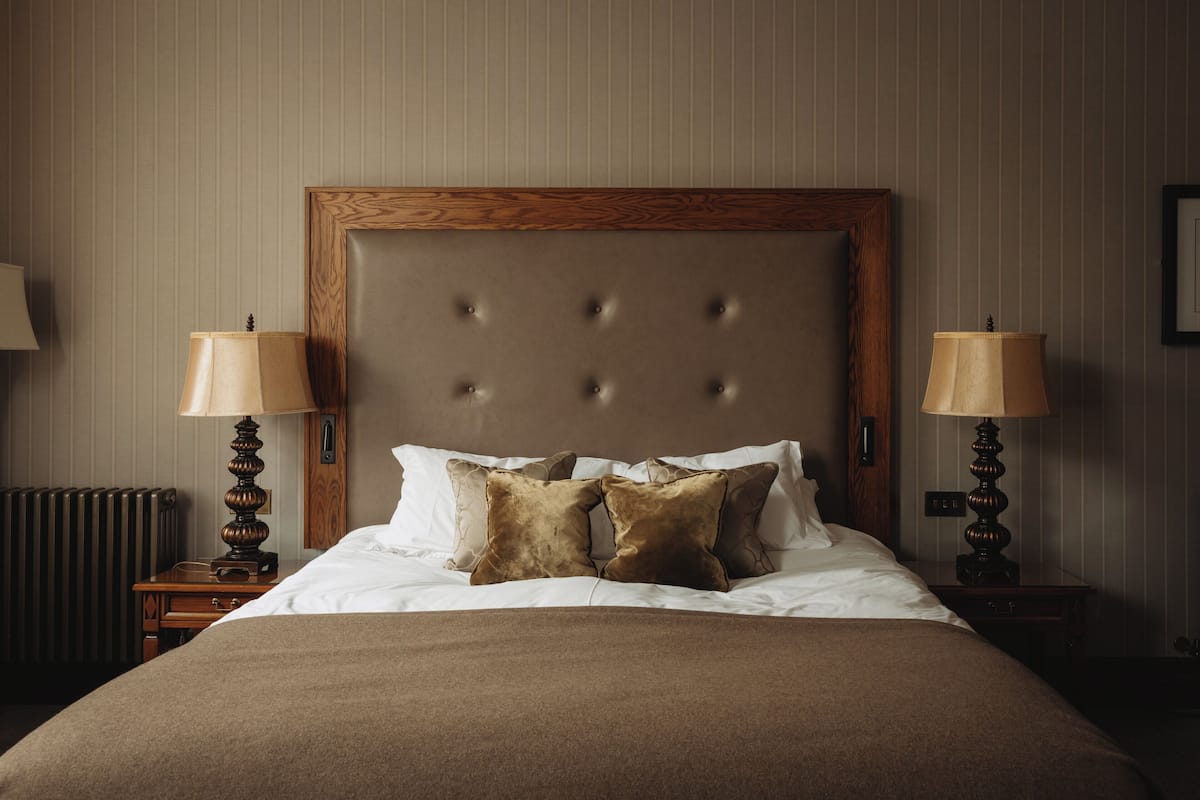 A neatly made bed with a wooden headboard, two bedside lamps, and a radiator.