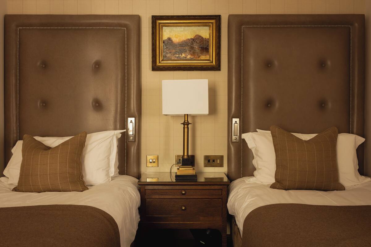 A hotel room with two beds, a nightstand with a lamp, and a painting on the wall.
