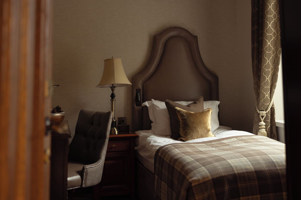 A hotel room with a bed, a chair, a nightstand, a lamp, and a window with curtains.