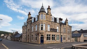 A corner building with a stone facade, a blue door, and a sign for the Station Hotel. - The Station Hotel (Aberlour)