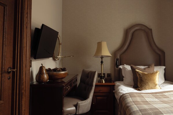 Una habitación de hotel con un escritorio de madera, una silla, una cama con cabecero, una lámpara y un televisor montado en la pared.