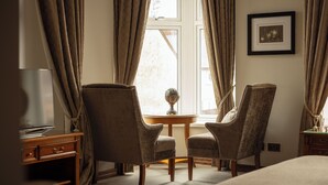 A hotel room with two upholstered armchairs, a small round table, a television on a wooden cabinet, and a framed picture on the wall. - The Station Hotel (Aberlour)