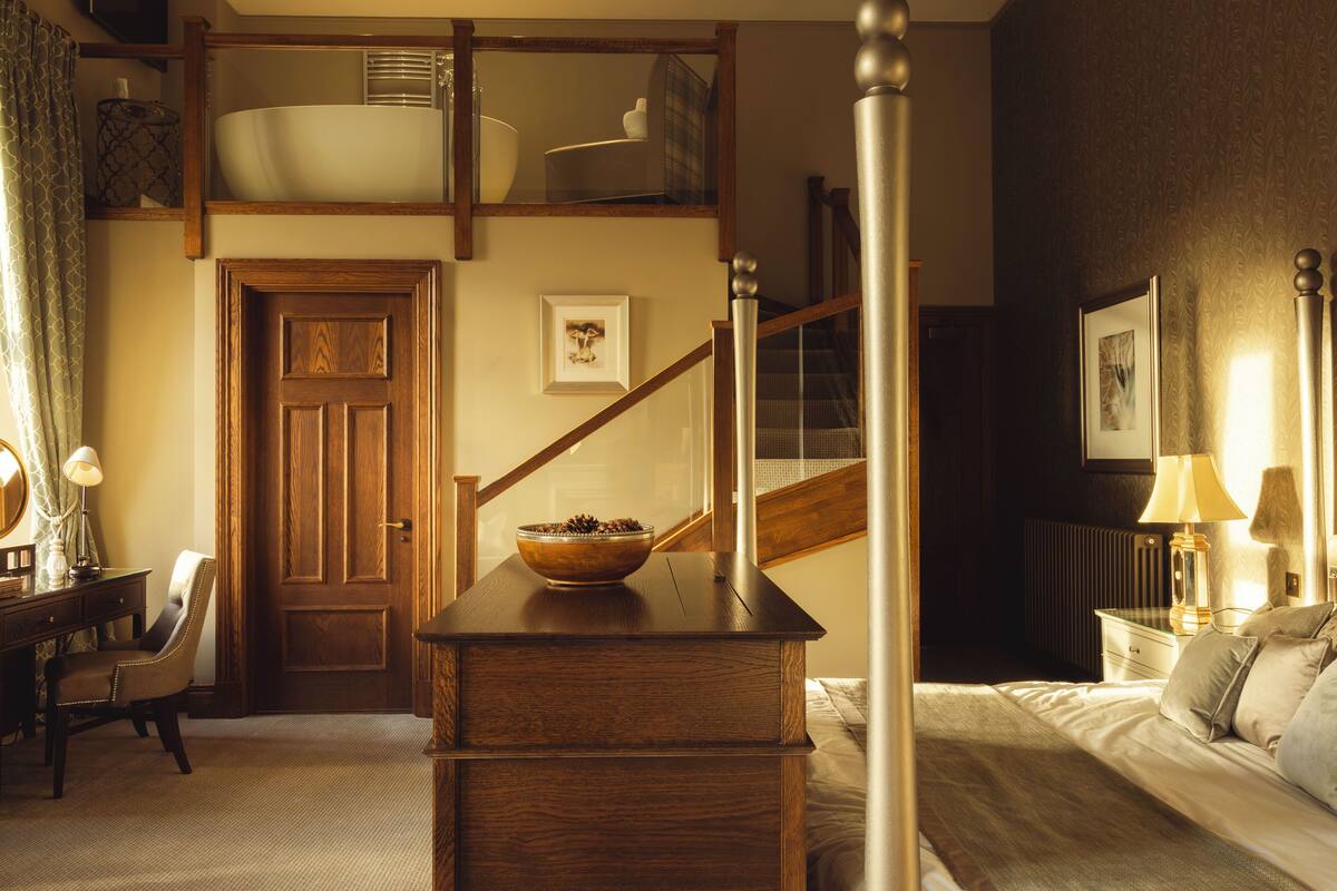 A bedroom with a wooden desk, a chair, a bed, a nightstand, a lamp, and a framed picture on the wall.