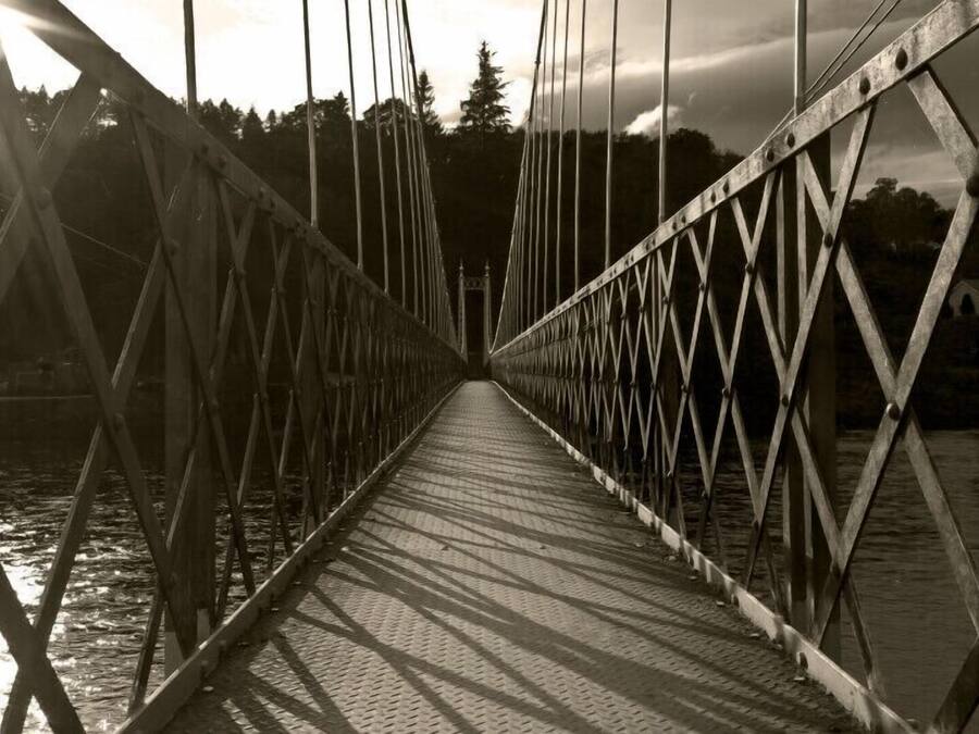 A suspension bridge with a metal framework and a paved walkway.
