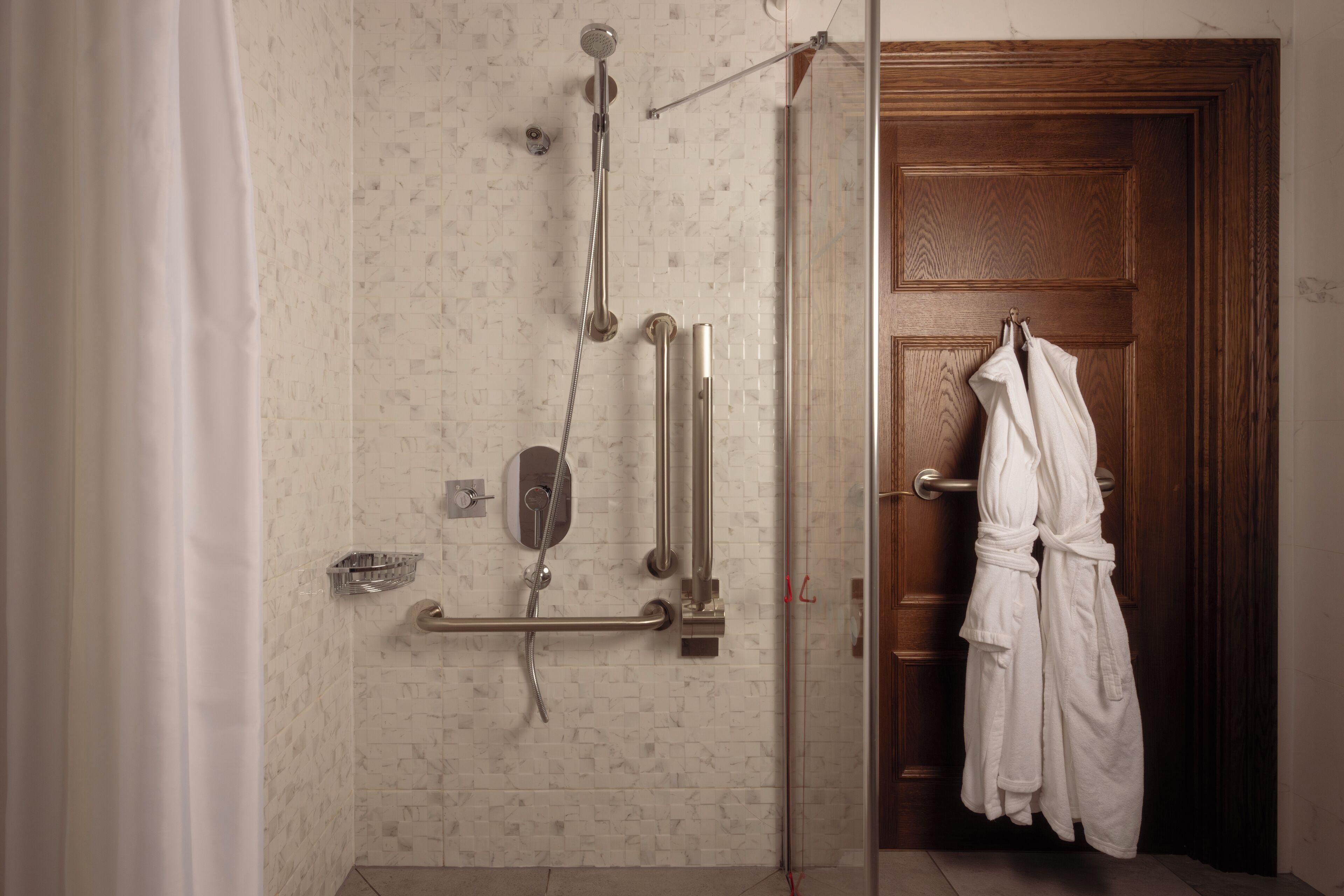 A shower area with a glass door, a wooden door, and a towel rack with white towels.