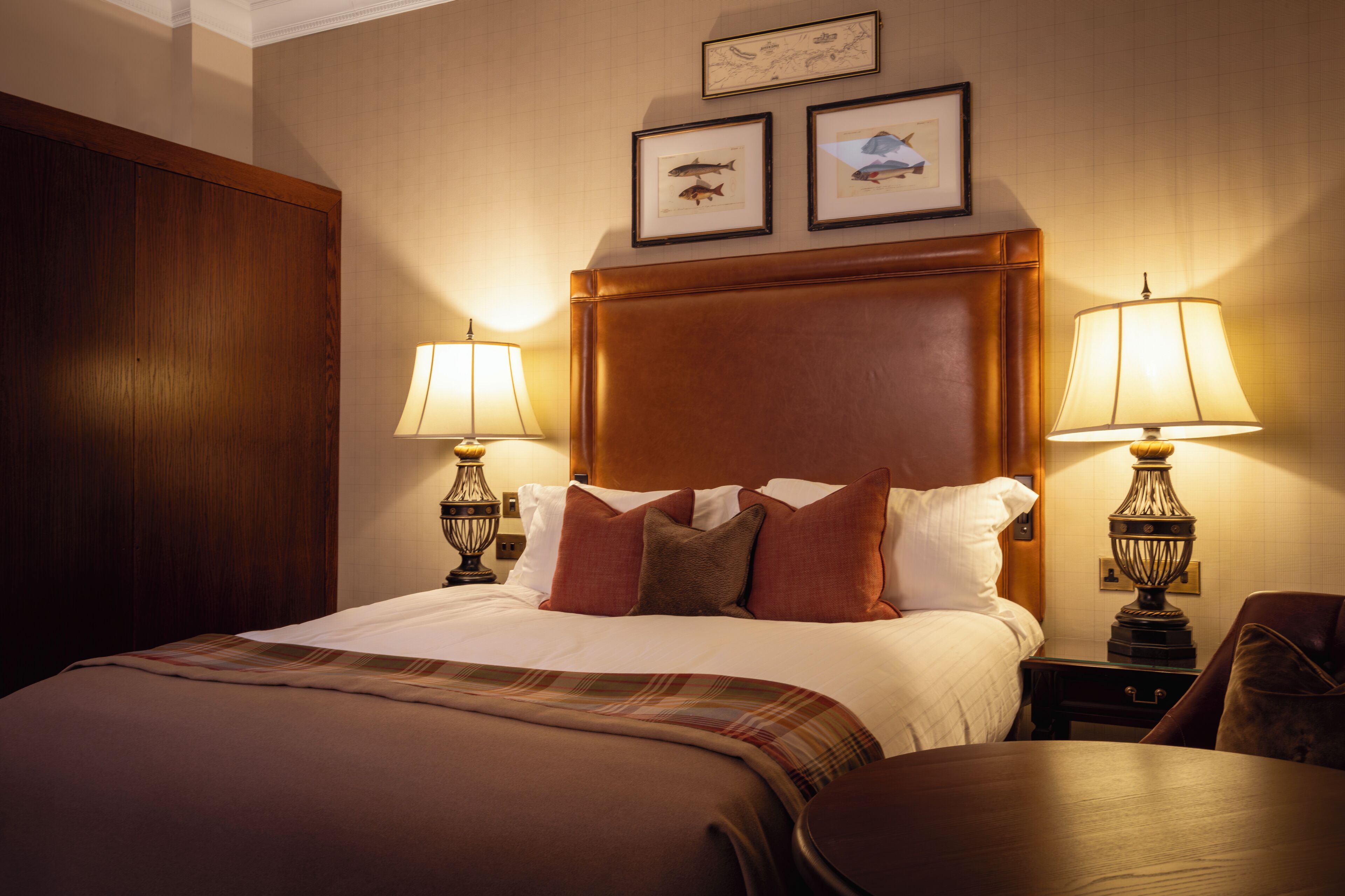 Een hotelkamer met een groot bed, twee bedlampjes, een houten hoofdbord en twee ingelijste foto's aan de muur.
