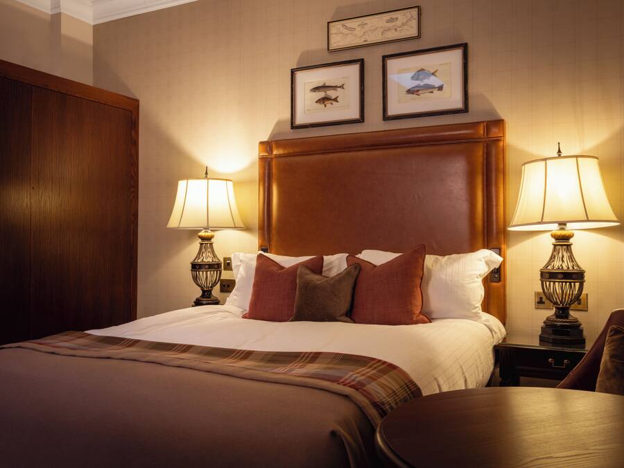 Quarto de hotel com uma cama grande, duas luminárias de cabeceira, um painel de cabeceira de madeira e dois quadros na parede.