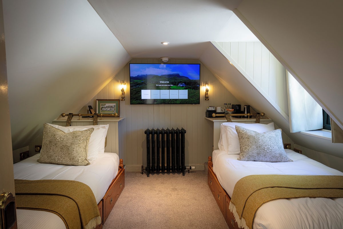 A bedroom with two beds, a TV mounted on the wall, and a radiator.