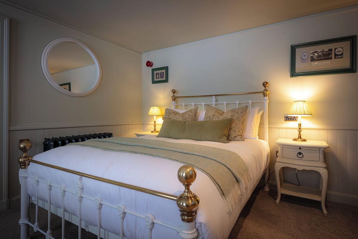 A neatly made bed with a white headboard and gold accents, flanked by two bedside tables with lamps.