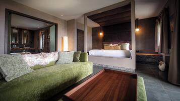 A modern hotel room with a green sofa, a wooden coffee table, a large bed with a headboard, a bathroom with a bathtub, and a large mirror.