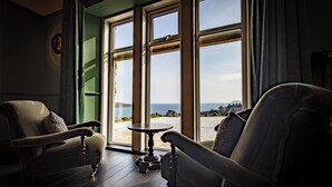 A room with two vintage-style armchairs, a small round table, and large windows offering a view of the sea. - The Flodigarry Hotel in the Skye  (Staffin)