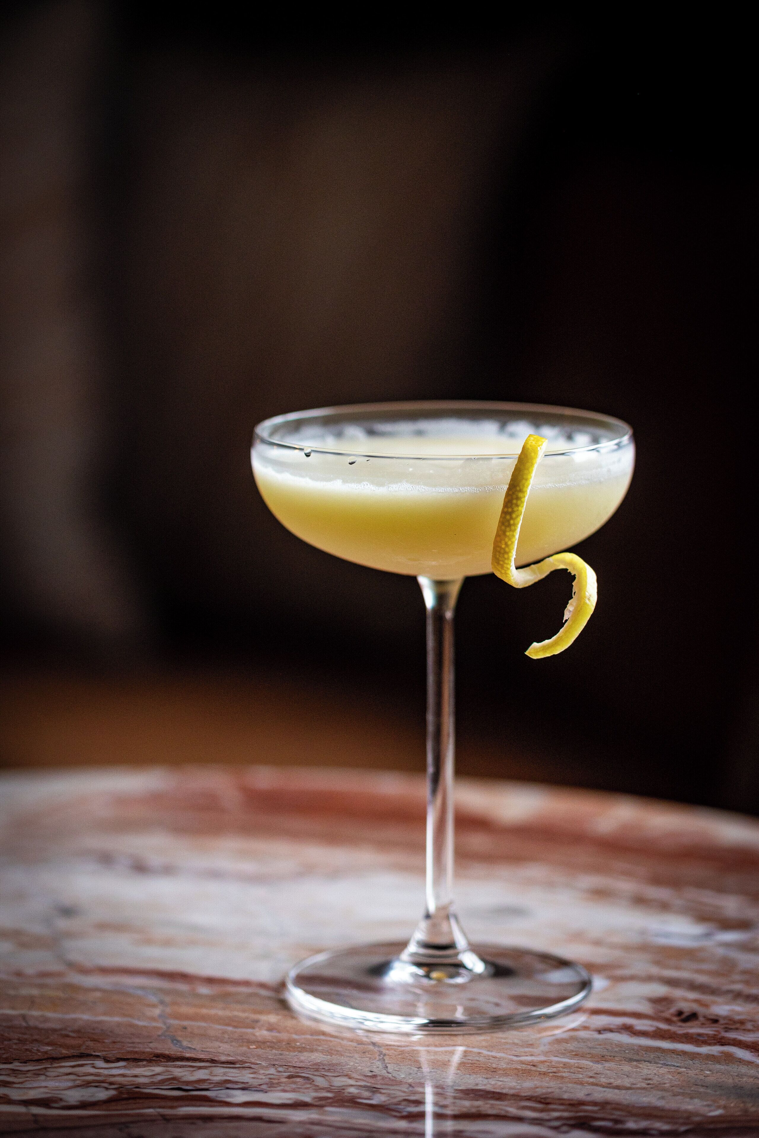 A cocktail in a martini glass with a lemon twist on a wooden table.