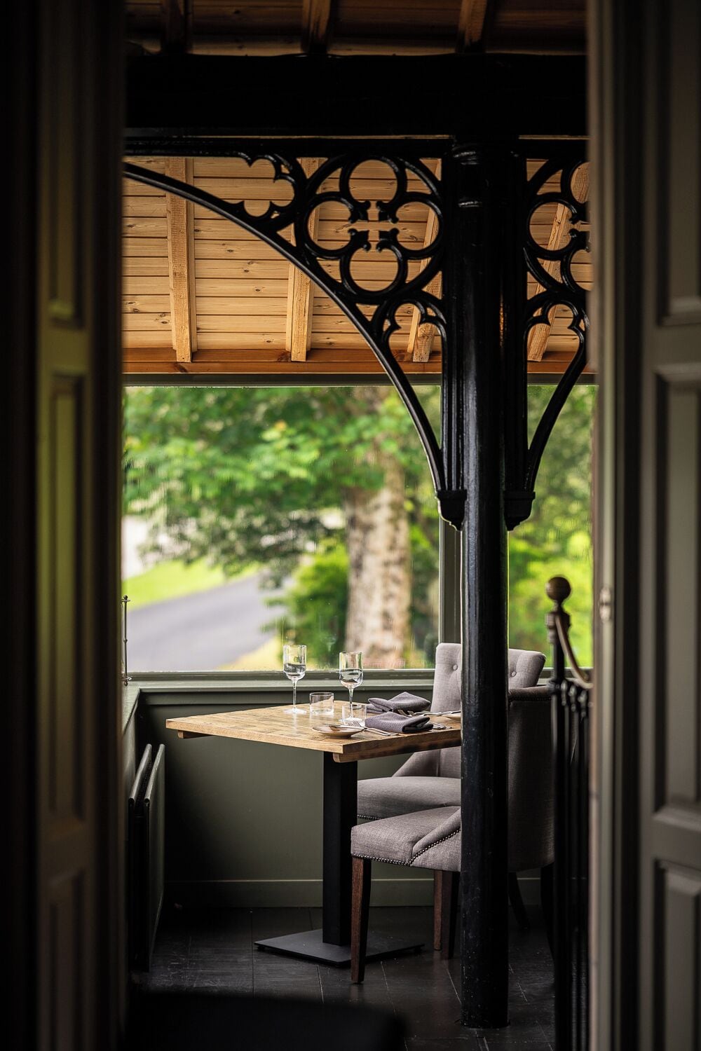 Comedor con una mesa lista para dos personas, una silla y vista a una calle arbolada.