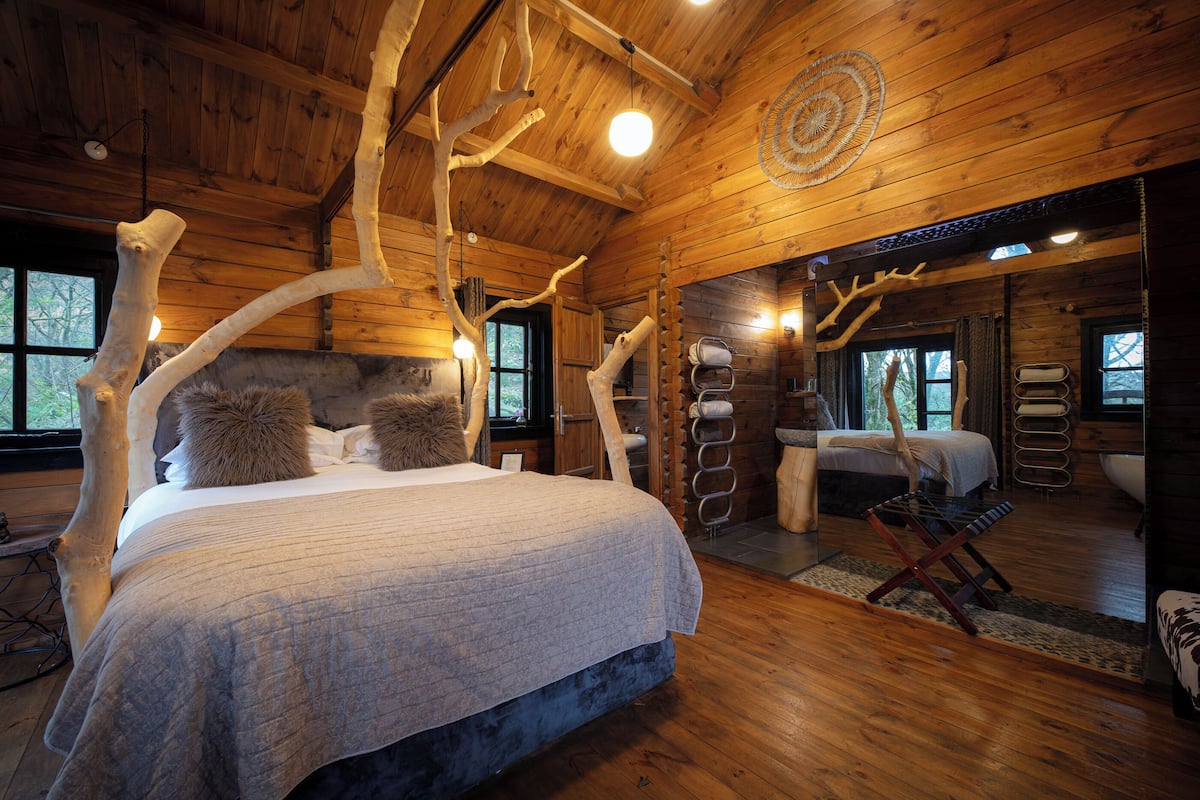 A log cabin bedroom with a large bed, a second bed, a sitting area, and a bathroom.