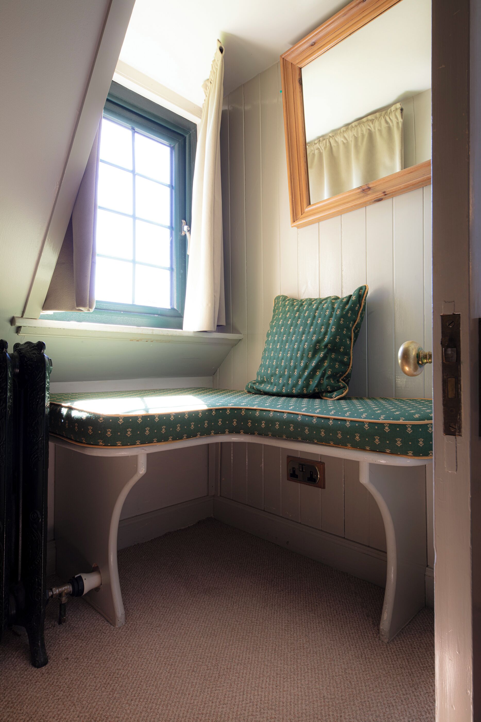 A corner bedroom with a window, a bed with a patterned bedspread, and a door.