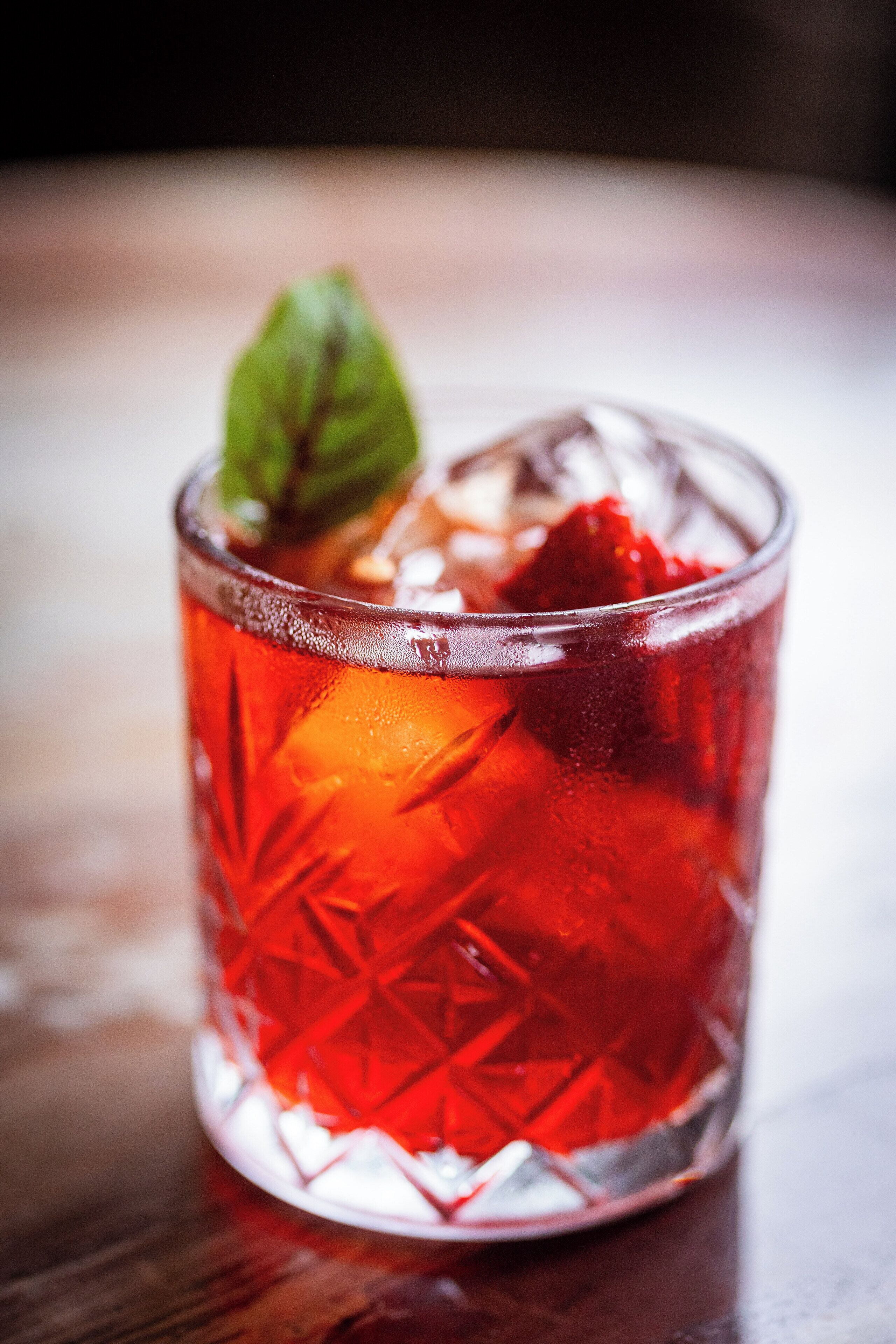 A clear glass with a geometric pattern, filled with a red liquid and ice cubes, with a mint leaf garnish.