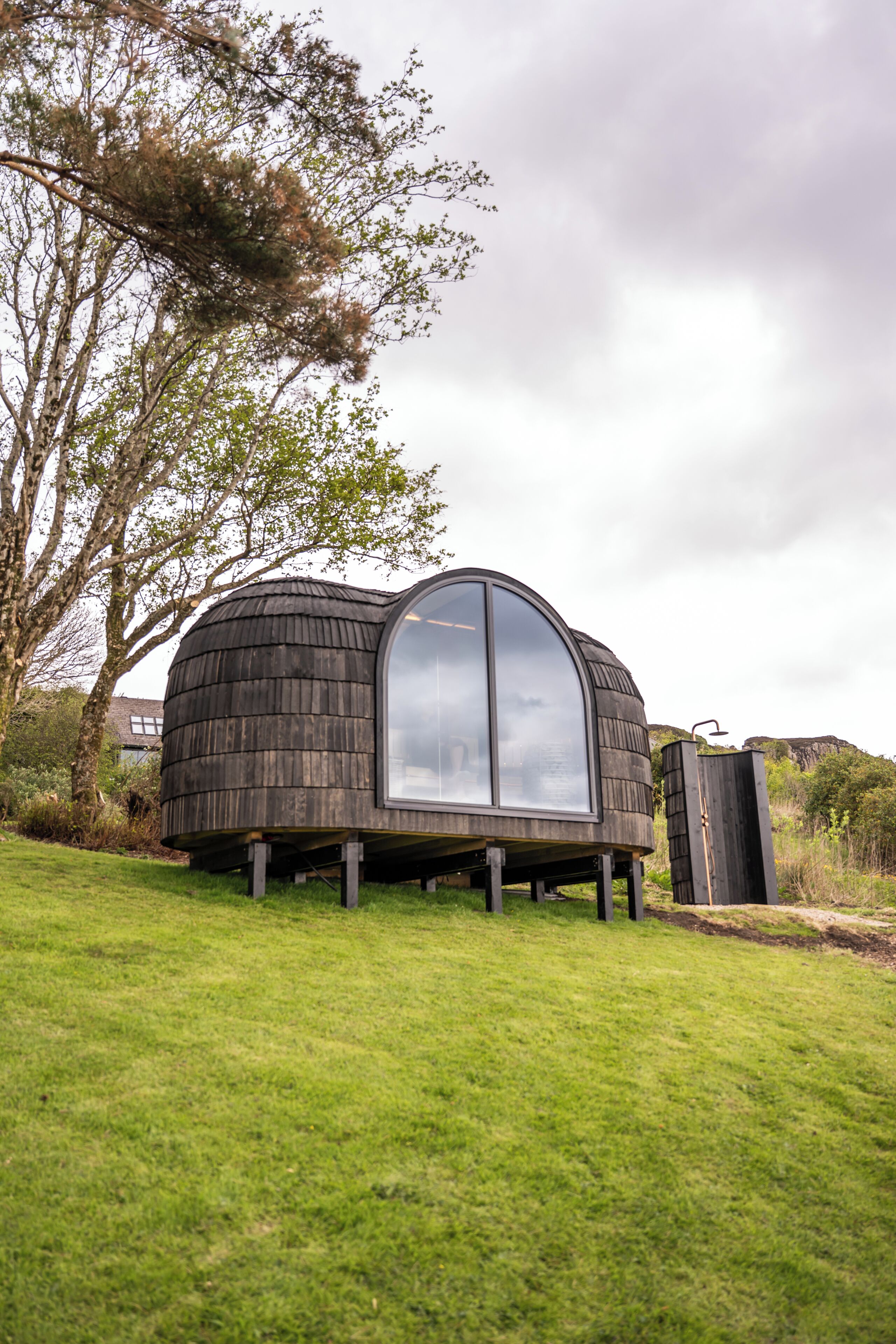 A modern, dome-shaped structure with a large glass window, situated on a grassy field with trees in the background.