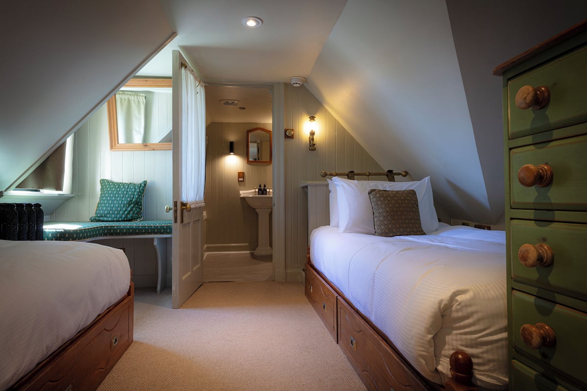 A bedroom with two beds, a green dresser, a window, and a bathroom with a sink and mirror.