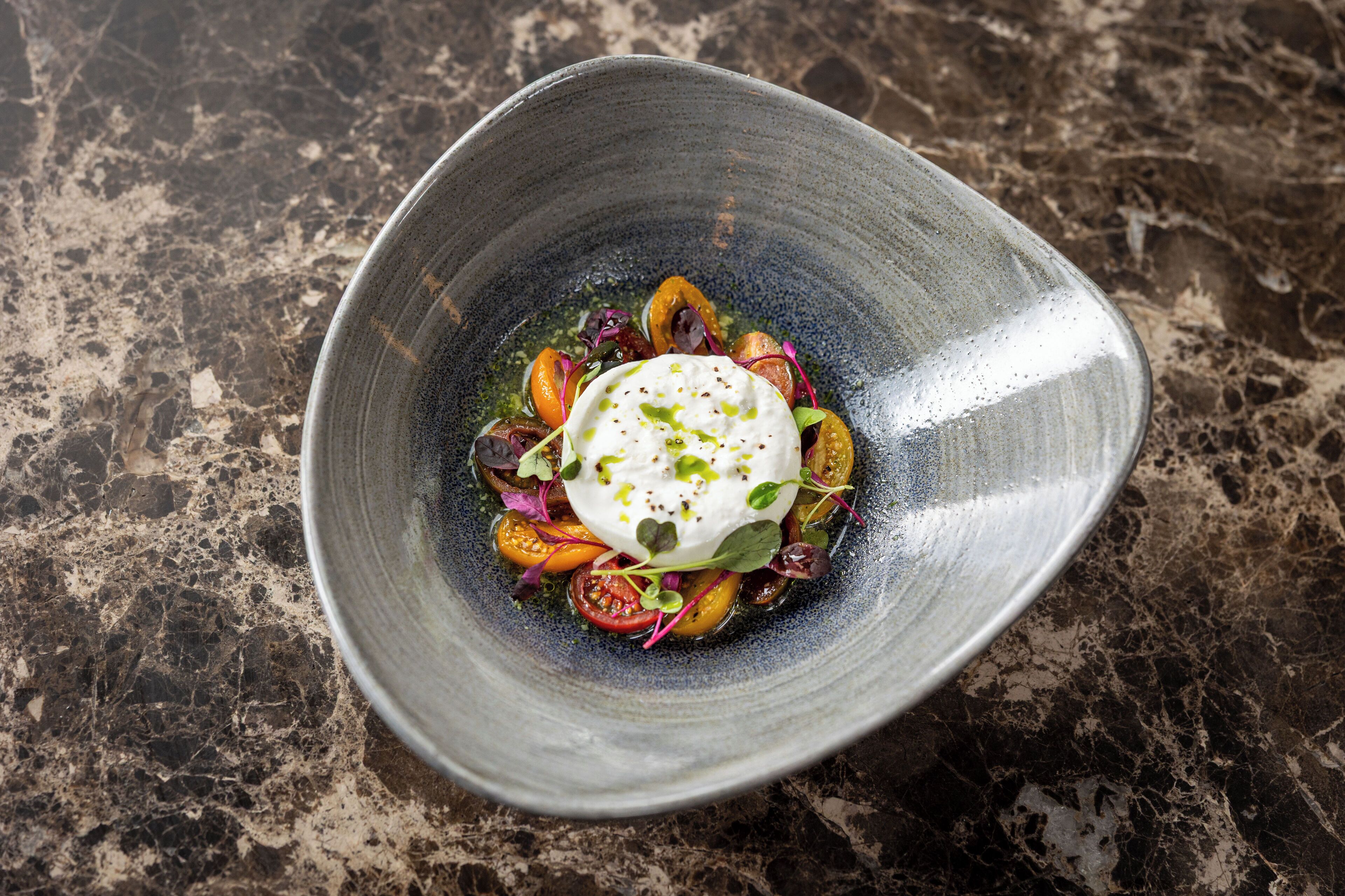 A dish with a white sauce and vegetables on a textured surface.