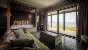 A modern bedroom with a large bed, a green sofa, and a view of the sea through large sliding doors. - The Flodigarry Hotel in the Skye  (Staffin)