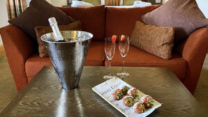 Habitación de hotel con un sofá marrón acogedor, un cubo de hielo metálico con una botella, dos copas de vino vacías y un plato de fresas.