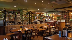Un restaurante acogedor con mobiliario de madera, una zona de bar y estantes con plantas y adornos.