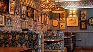 Interior de restaurante con papel tapiz estampado, varias obras de arte enmarcadas y asientos tradicionales.