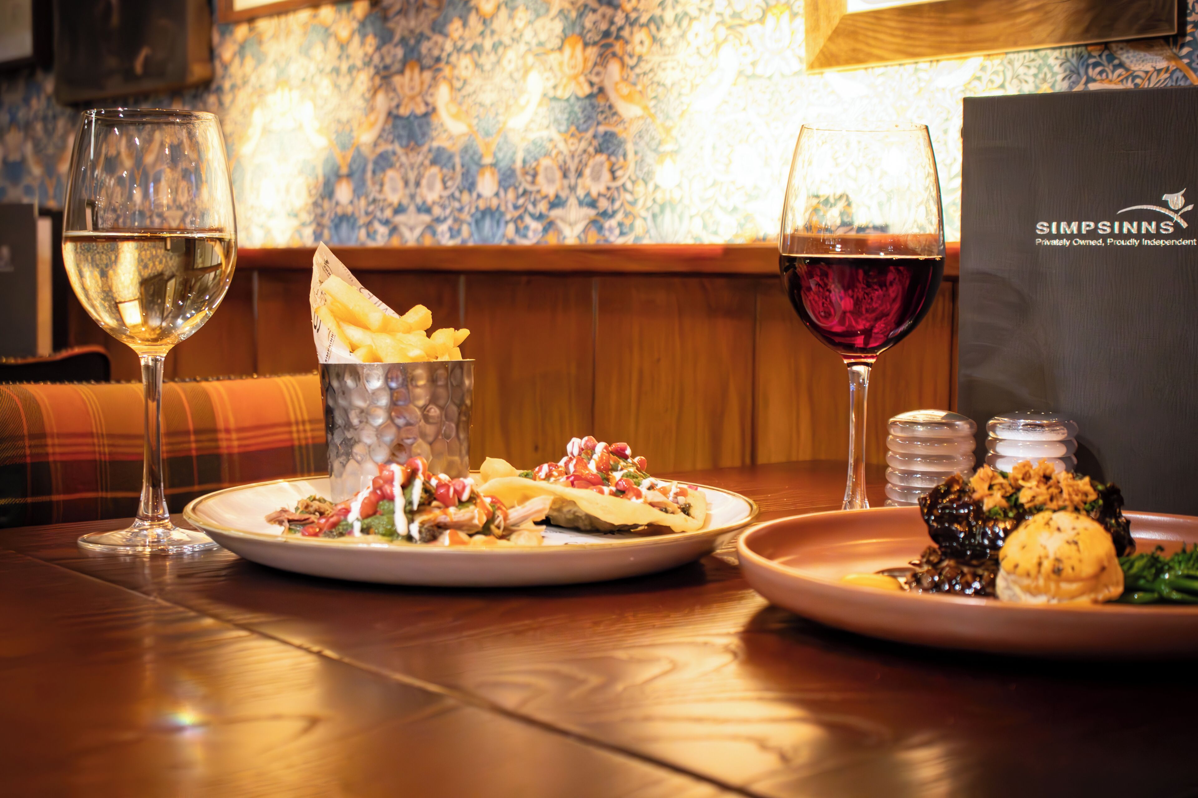 Une table à manger avec deux assiettes de nourriture, deux verres de vin et un présentoir à menus.