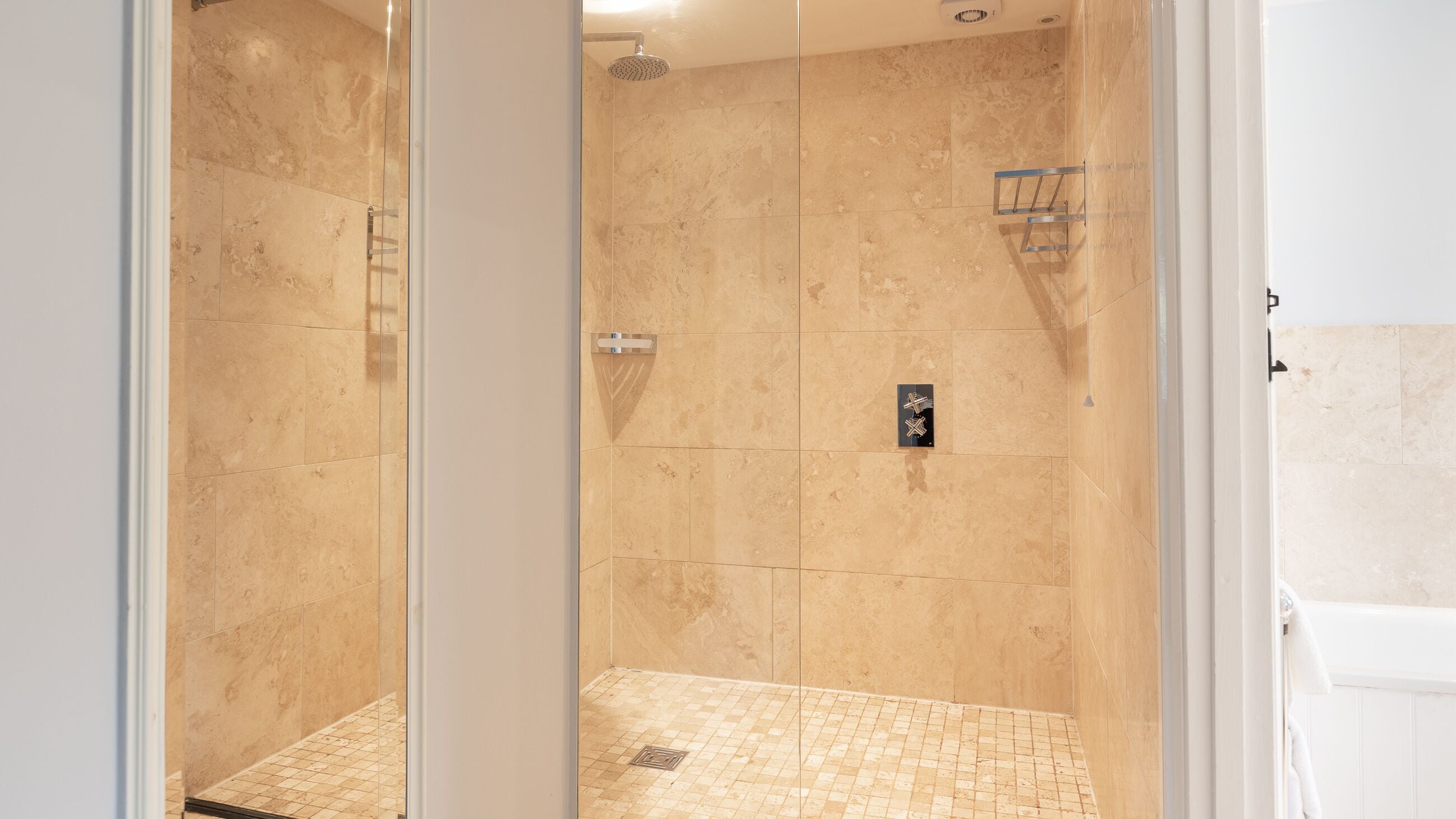 Box doccia in vetro con piastrelle beige e soffione.